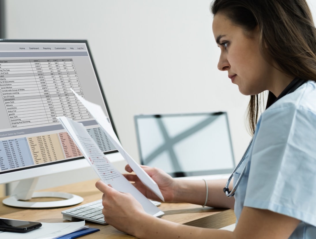 Healthcare provider looks over patient paperwork with their compute monitor showing data in front of them.