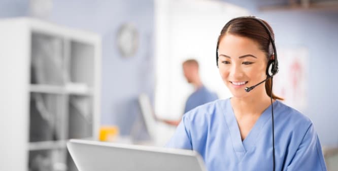 Nurse wearing a headset looks at her computer screen.