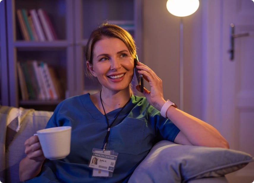 A nurse on a phone holding a white coffee cup.