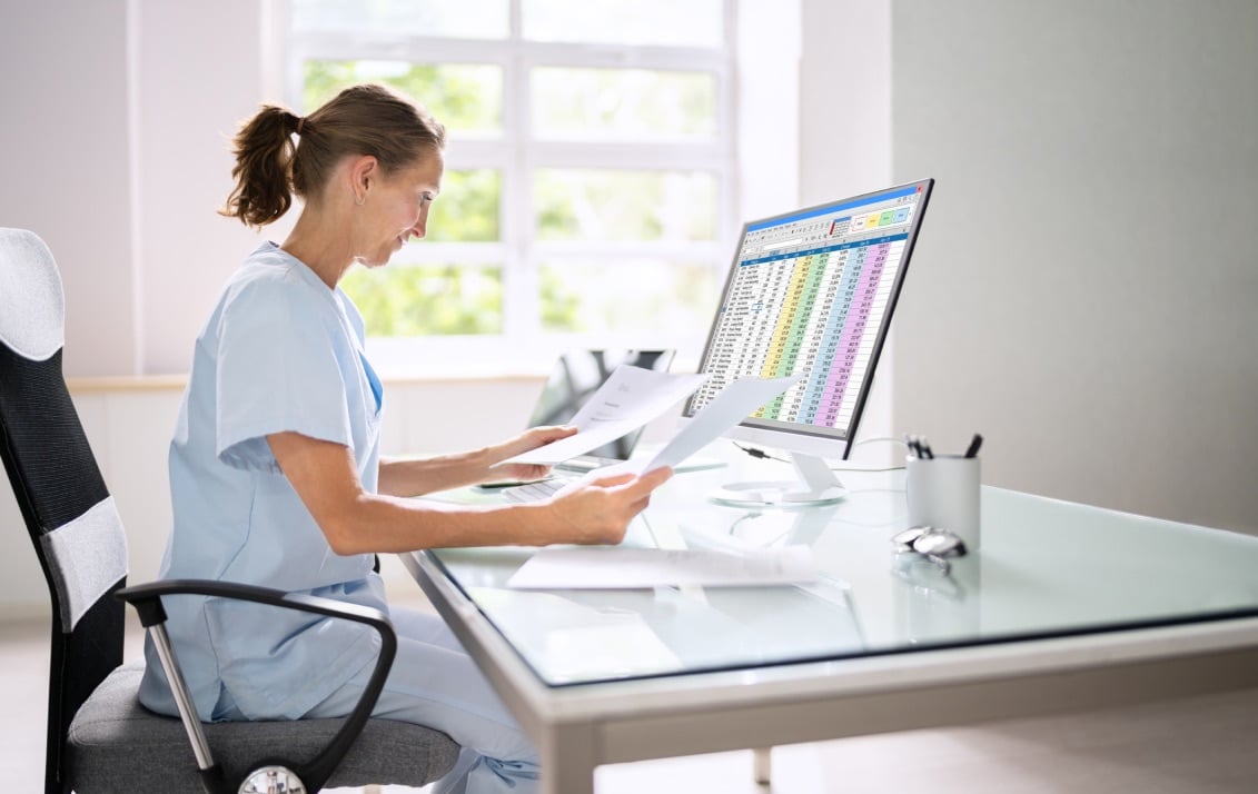 Medical professional holds out two pieces of paper with their monitor screen showing input details.