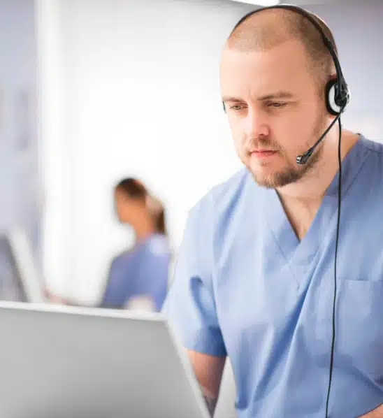 Looking at their computer screen, wearing a headset, a medica provider reviews patient files.