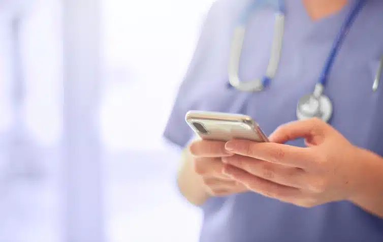 Nurse stands, holding their cellphone in their hands as they type on it.