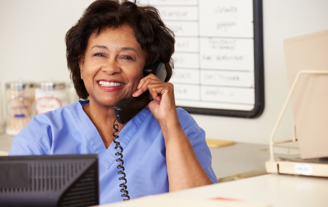 Talking on a corded phone, a nurse smiles as she chats with a patient.