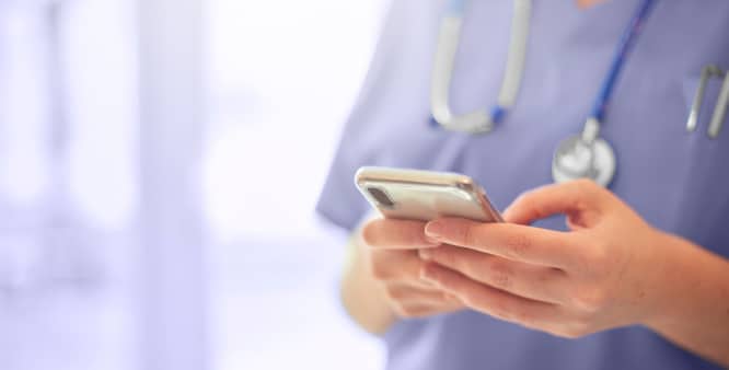 Healthcare provider holding a cellphone, standing in a medical building.