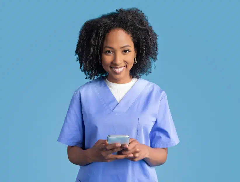 A medical provider stands in front of a blue background holding a cellphone in front of them.