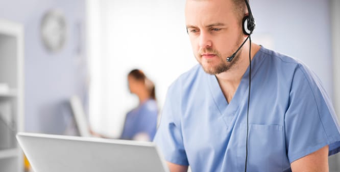Healthcare professional, wearing a headset, looks at their computer screen as they speak with a patient.