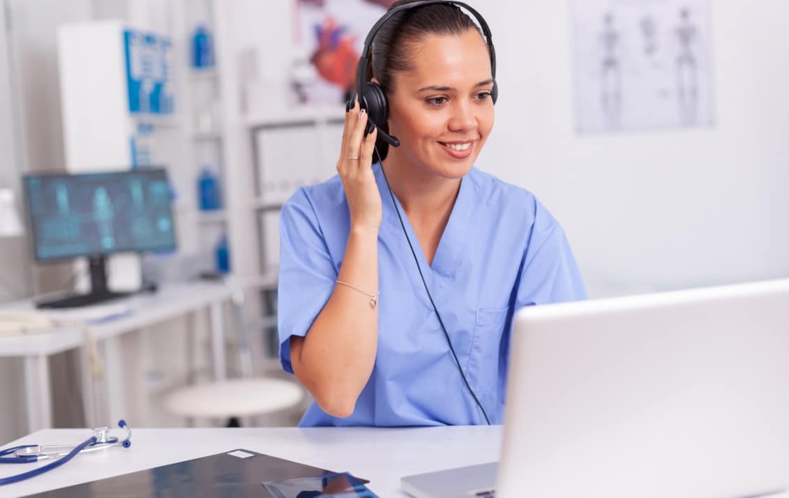 A nurse talks on a headset while looking at their laptop.